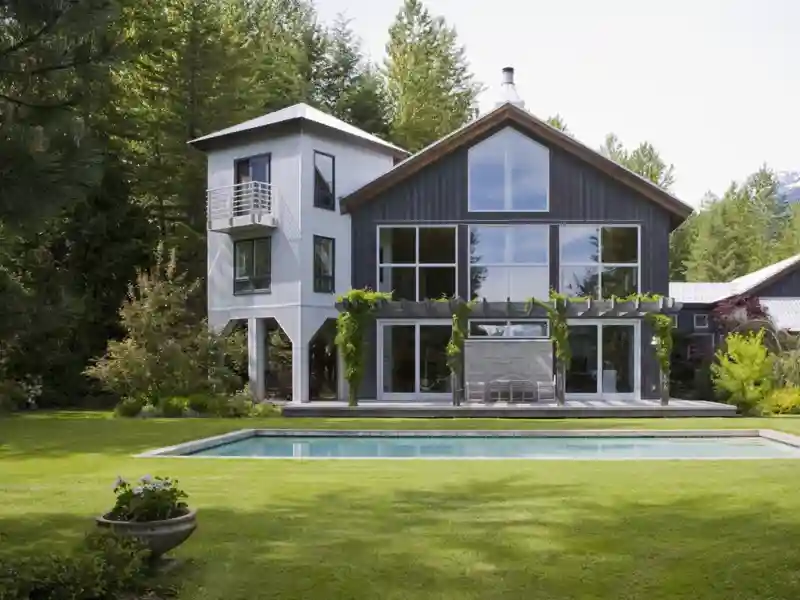 Large modern house in the woods overlooking a pool.