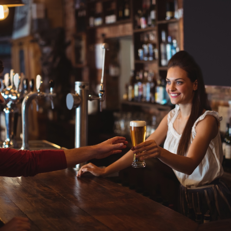 Female bar tender giving glass of beer to customer at bar counter