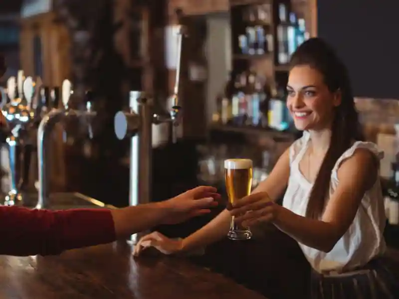 Female bar tender giving glass of beer to customer at bar counter