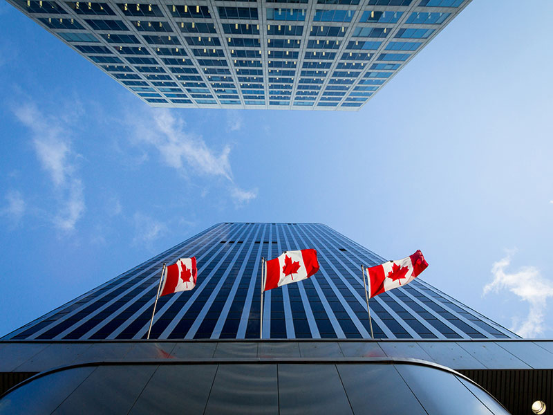 Looking up at a building with three Canadian flags flying.