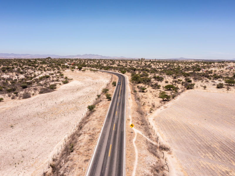 A lone car drives along a desolate Mexican desert road.