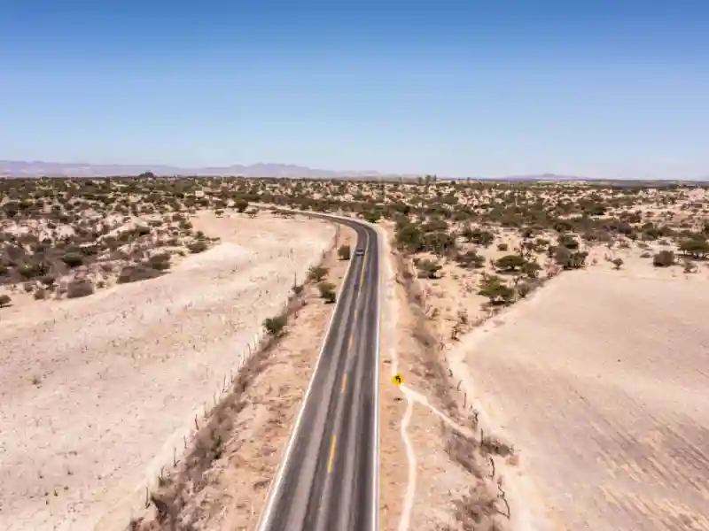 A lone car drives along a desolate Mexican desert road.